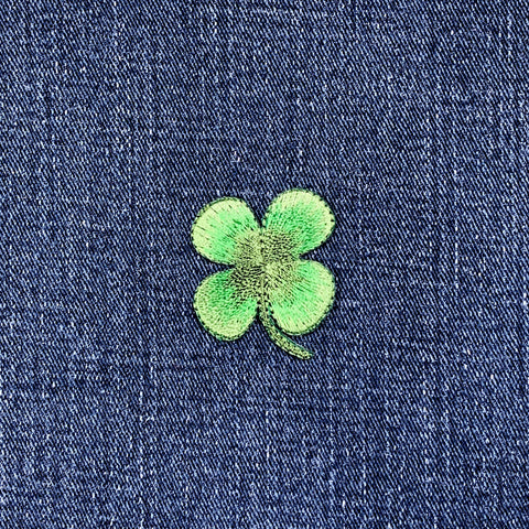 Green four-leaf clover patch on blue denim fabric