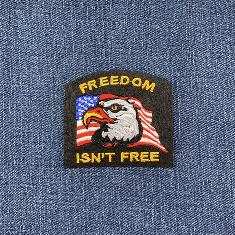 A patch featuring an eagle with a American flag in the background, with the text 'FREEDOM ISN'T FREE' on it, displayed on a denim background