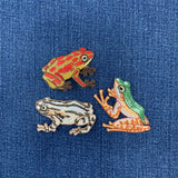 Three embroidered frog patches on a blue fabric background
