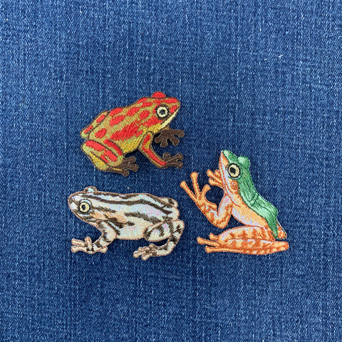 Three embroidered frog patches on a blue fabric background