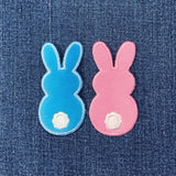 Two bunny-shaped patches, one blue and one pink, on a denim background.