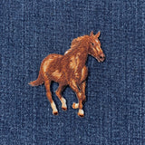 An embroidered iron-on patch featuring a running brown horse with a brown mane and tail, set against a dark blue denim fabric background.