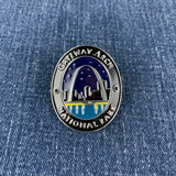 An oval enamel Walking Stick Medallion featuring a Gateway Arch National Park design, displayed on a blue denim fabric background.