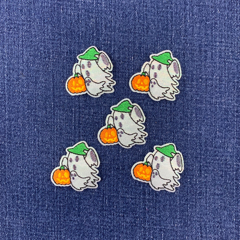 Five identical embroidered patches of a cute cartoon ghost holding an orange pumpkin, decorated with a green hat, arranged on a blue denim fabric background.