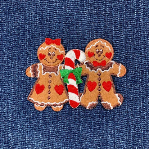 Two gingerbread people with a candy cane on a denim background