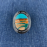 An oval enamel Walking Stick Medallion featuring the Glen Canyon National Recreation Area landscape, displayed on a blue denim fabric background.