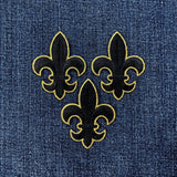Three black and gold fleur-de-lis patches on denim fabric.