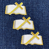 Three embroidered patches of open bibles with gold crosses on a denim background