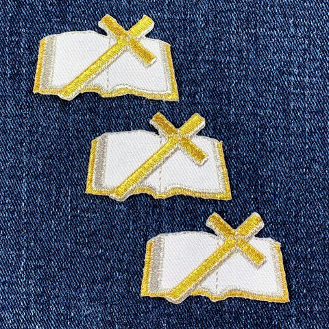 Three embroidered patches of open bibles with gold crosses on a denim background