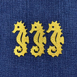 Three gold seahorses embroidered on a blue fabric background