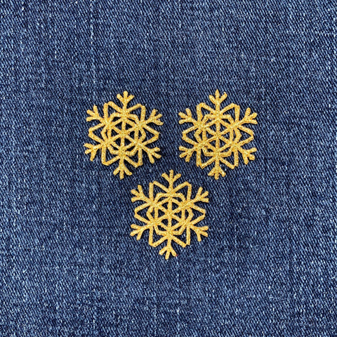 three gold snowflake patches on a denim background