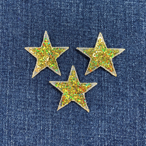 Three glittery gold star-shaped patches on a denim background