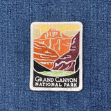 A rectangular embroidered patch depicting the Grand Canyon in shades of orange, brown, and purple. The bottom section is black with the text 'GRAND CANYON NATIONAL PARK' stitched in gray on a denim background