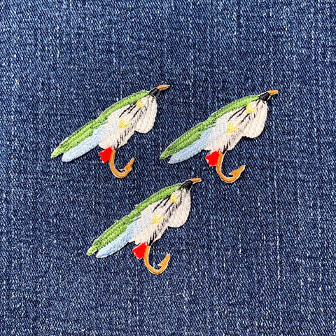 Three fishing fly patches on a denim background