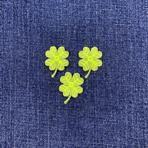 Three green four-leaf clover patches on blue denim fabric