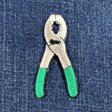 Patch of pliers with green handles on denim fabric