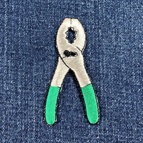 Patch of pliers with green handles on denim fabric