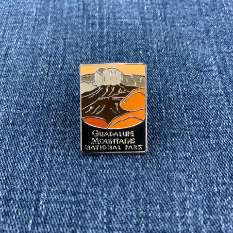 A pin badge featuring an illustration of Guadalupe Mountains National Park with a predominantly orange and black color scheme on a denim background