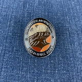 An oval enamel Walking Stick Medallion featuring a landscape design of Guadalupe Mountains National Park, displayed on a blue denim fabric background.