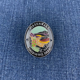 An oval enamel medallion for Haleakala National Park, featuring a detailed landscape illustration of a lake, mountains, and a bird, set against a blue denim fabric background.