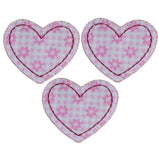 Three pink and white heart-shaped applique patches with a floral daisy pattern on a satin print background.