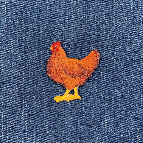 Embroidered chicken applique patch in brown and yellow colors with a red comb and wattle on a denim background.