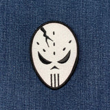 A patch depicting a hockey goalie mask with a cracked face design on a denim background