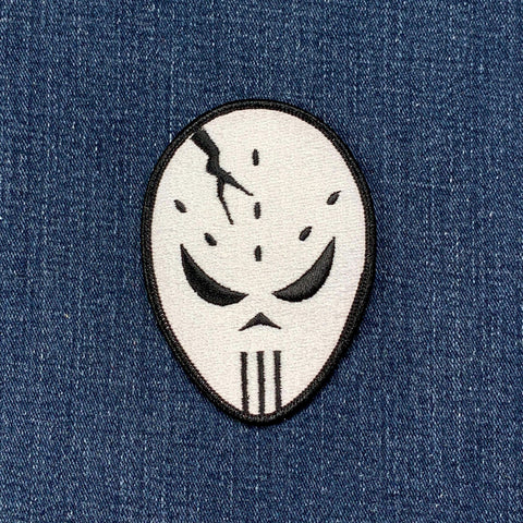 A patch depicting a hockey goalie mask with a cracked face design on a denim background