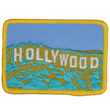 A rectangular embroidered patch with the text 'Hollywood' on it, predominantly blue and yellow in color, with a mountain-like design in the background.