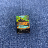 A collectible pin representing Hot Springs National Park with an illustration of a pool and waterfall on a denim background