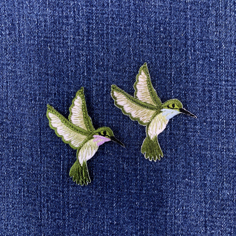 Two embroidered hummingbird patches on a denim background