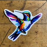 A colorful vinyl decal of a hummingbird with a vibrant and artistic design, placed on a wooden surface.