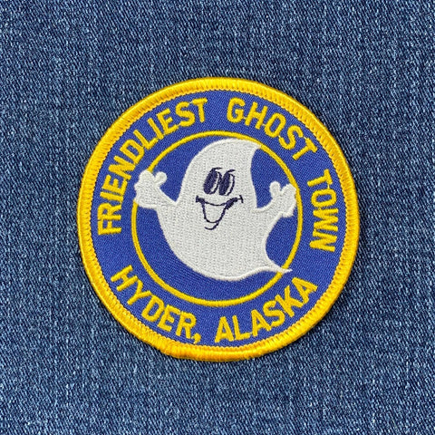 Round blue patch with a smiling ghost character, text 'FRIENDLIEST GHOST TOWN HYDER, ALASKA', and a yellow embroidered border on a denim background