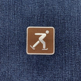 A square brown patch with a white outline and a white ice skating symbol, placed on a blue denim background.