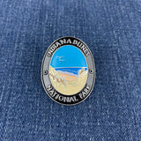 A round walking stick medallion with an illustration of a beach and Lake Michigan, and the text 'Indiana Dunes National Park' on a denim background