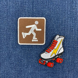 Two embroidered patches on a blue denim background: a square brown patch with a white roller-skating figure icon, and an embroidered roller skate in white with red laces and wheels plus a yellow lightning bolt.