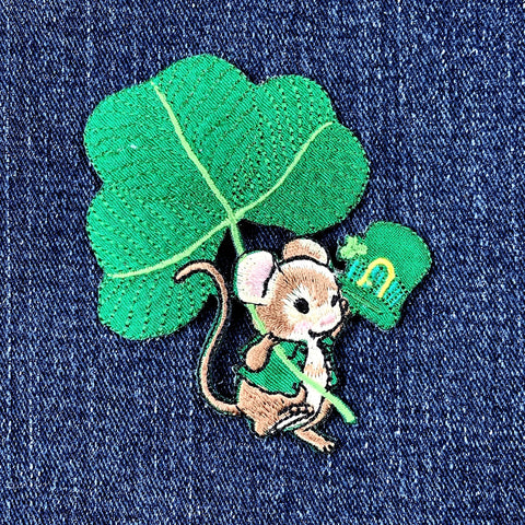 an embroidered patch featuring a mouse, a shamrock and a green hat representing Saint Patrick's Day, displayed on a denim background