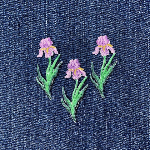 Embroidered purple iris flower patches on a denim fabric background