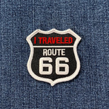 Shield-shaped embroidered patch resembling a U.S. highway sign, reading "I TRAVELED ROUTE 66" in white and red text on a black background.