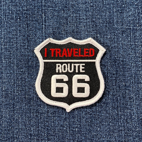 Shield-shaped embroidered patch resembling a U.S. highway sign, reading "I TRAVELED ROUTE 66" in white and red text on a black background.