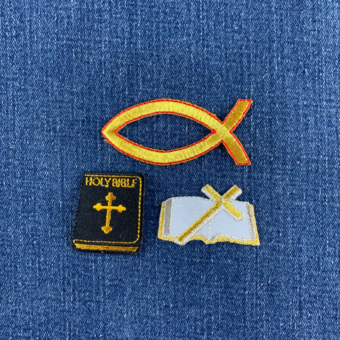 Three embroidered patches on a blue denim fabric background: a gold Ichthys fish patch, a black Holy Bible book patch with gold embroidery, and an open bible patch with a gold cross on a white page.