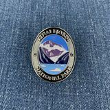 An oval enamel Walking Stick Medallion featuring Kenai Fjords National Park, displayed on a blue denim background.