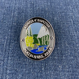 An oval metal enamel Walking Stick Medallion featuring a landscape of Kings Canyon National Park with a mountain, trees, and river, bordered by the text 'KINGS CANYON NATIONAL PARK' on a blue denim background.