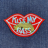 Embroidered patch shaped like red lips with light blue trim, featuring a yellow striped bass and the light blue text "KISS MY BASS."
