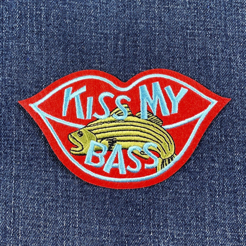 Embroidered patch shaped like red lips with light blue trim, featuring a yellow striped bass and the light blue text "KISS MY BASS."