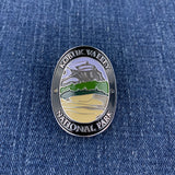 An oval metal Walking Stick Medallion featuring a landscape design of Kobuk Valley National Park, displayed on a blue denim fabric background.