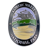 Oval Kobuk Valley National Park medallion with a black border, silver lettering, and a multicolor landscape design featuring gray mountains, green hills, and beige foreground on a white background.