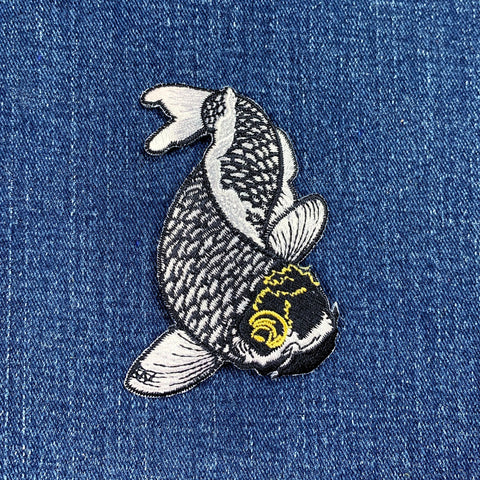 A embroidered black and white koi fish applique patch on a denim background