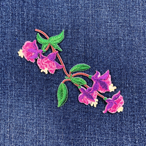 Embroidered pink flower patches with green leaves on denim fabric