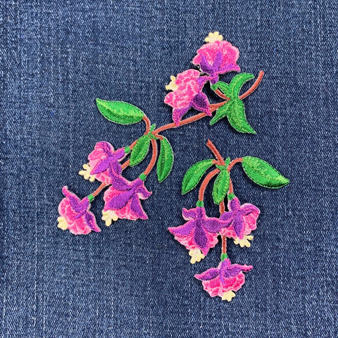 Two embroidered pink flower patches with green leaves on denim fabric